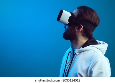 Side View Of Serious Bearded Guy In VR Headset Experiencing Another World In Studio, Isolated Over Blue Background