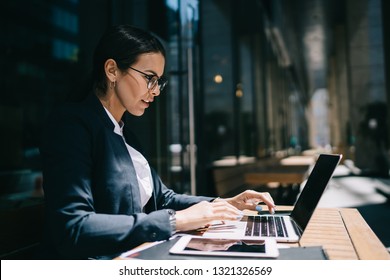 Side view of serious female economist working online with accounting documents on modern laptop device during sunny day in street cafeteria, caucasian businesswoman typing name for media files