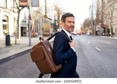 Side view of serious middle aged male entrepreneur in suit and with backpack walking across road while commuting to work - Shutterstock ID 2245569921