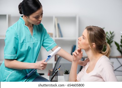 Side View Of Serious Nurse Holding Clipboard With Diagnosis And Talking With Pensive Young Patient