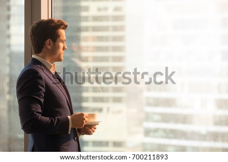 Side view of serious pensive director of prosperous company enjoying cup of coffee in the morning, thoughtful businessman in suit looking through big office window at dawn sunrise city, copy space