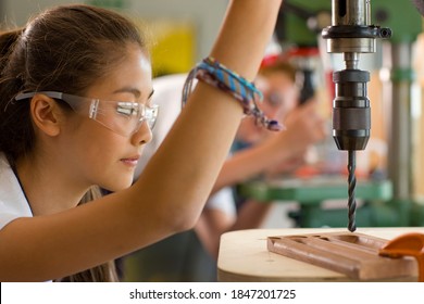 A side view of a serious student wearing safety glasses while using the drill machine in a vocational school