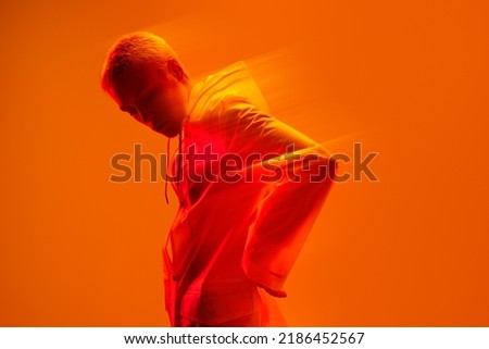 Side view of serious stylish young female model with short blond hair in raincoat looking down against bright orange background