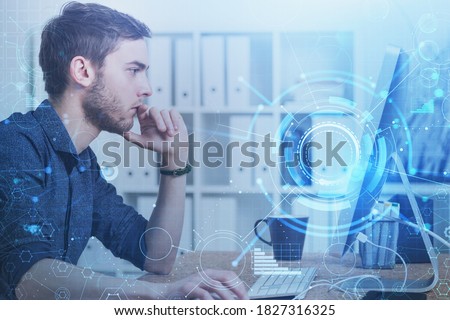 Side view of serious young businessman using his computer in blurry office with double exposure of HUD network interface. Toned image