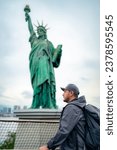 Side view of serious young Hispanic male tourist in jacket and cap with backpack standing near Odaiba Statue of Liberty and admiring city during trip in Tokyo Japan