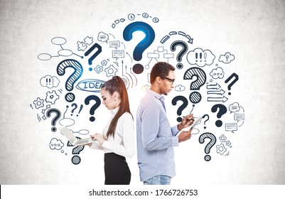 Side view of serious young woman with laptop and thoughtful African American student taking notes near concrete wall with question marks and business sketch drawn on it. Concept of education - Powered by Shutterstock