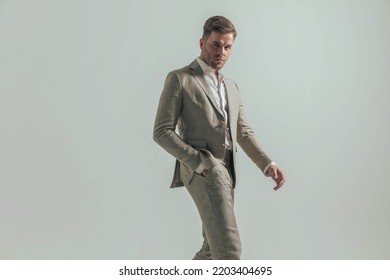 Side View Of Sexy Man With Open Collar Shirt Holding Hand In Pocket And Walking In Front Of Grey Background In Studio