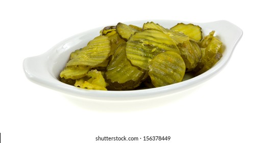 Side View Of A Shallow Dish Filled With Bread And Butter Pickles On A White Background.