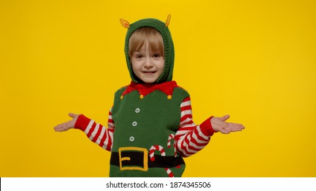 Side View Shocked Blonde Kid Girl In Christmas Elf Santa Helper Costume. Child Turn Round Look At Camera And Say Ask Question What Isolated On Yellow Background. People Sincere Emotions