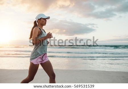 Side view shot of beautiful young woman in sportswear jogging on beach. Female runner jogging on outdoors on beach.