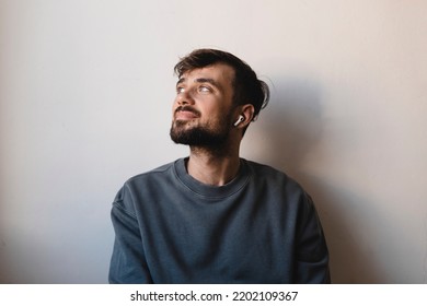 Side view shot of brunette young man listening to music and wear the wireless headphone, sitting  isolated on a white wall background. Handsome man look side up. - Powered by Shutterstock