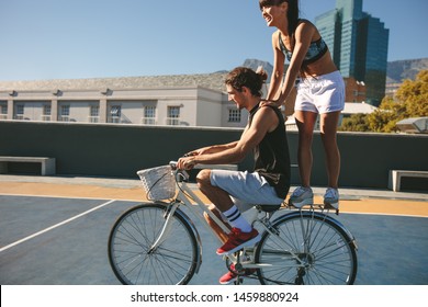 Side view shot of couple having fun while riding a bike outdoors. Man and woman performing some stunts while cycling. - Powered by Shutterstock