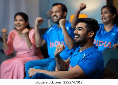 Side view shot of Group of family member shouting as India to support Indian Cricket Team while watching on tv at home - concept of Energetic fans, Cheering Family and Team Spirit.