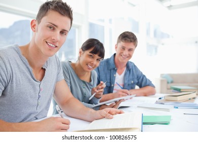 A Side View Shot Of A Group Of Young Adults With Their Homework On The Table As They All Look Into The Camera