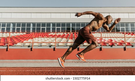 Side view shot of male sprinter running on the sport track. Athlete runner doing workout at the stadium