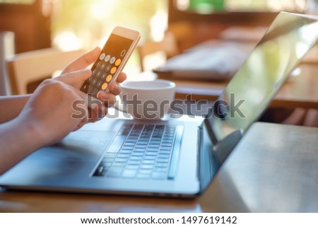 Side view shot of a man's hands using calculation in smart phone in interior, rear view of business man hands busy using cell phone at office desk and labtop that has a laptop and coffe cup