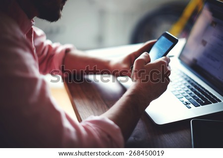 Side view shot of a man's hands using smart phone in interior, rear view of business man hands busy using cell phone, young male student typing on phone sitting at wooden table focus on the hand