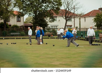 A side view shot of a senior woman taking her shot in a game of lawn bowling, surrounded by other seniors in the community.
