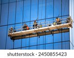 Side view shot of three window washers on a hanging scaffold on a commercial building with blue glass