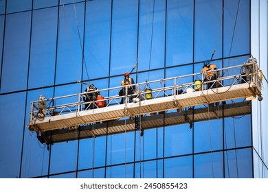 Side view shot of three window washers on a hanging scaffold on a commercial building with blue glass