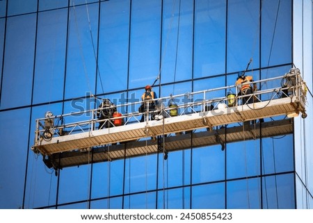 Side view shot of three window washers on a hanging scaffold on a commercial building with blue glass