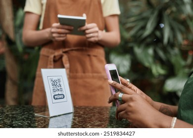Side view shot of unrecognizable cafe visitor scanning qr-code to open online menu while unrecognizable waitress waiting for order