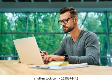 Side view shot of young handsome businessman with glasses and beard working on laptop at office desk - Shutterstock ID 1850694442