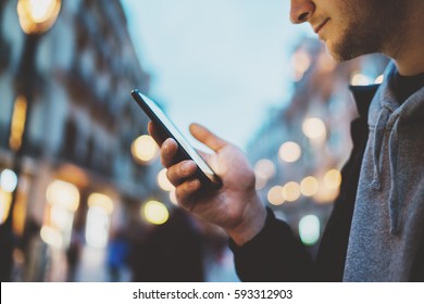 Side view shot of young smiling man using smartphone at night city street, bokeh lights, hipster guy chatting with friends at social networks via cellphone outdoor, visual effects - Powered by Shutterstock