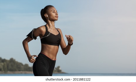 Side view shot of young woman in sportswear jogging on beach. African-american female jogger runner running outdoors. Active lifestyle concept