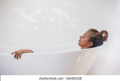 Side view shot of young woman lying in bathtub with her eyes closed. Female relaxing in bathtub. - Powered by Shutterstock