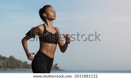 Side view shot of young woman in sportswear jogging on beach. African-american female jogger runner running outdoors. Active lifestyle concept