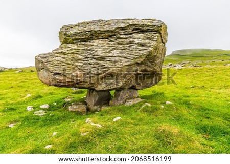 A side view showing a glacial erratic supported on the limestone pavement on the southern slopes of Ingleborough, Yorkshire, UK in summertime