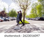 side view of a sightless man walking on the zebra crossing using his cane and a woman providing guidance.