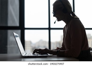 Side View A Silhouette Of Female Call Center Employee Using A Headset And Laptop For Online Communication With Customers, A Woman Talking Into Microphone And Typing On The Keyboard, Checks And Marks