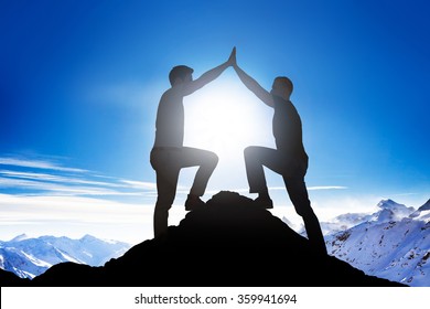 Side view of silhouette male friends giving high five on mountain peak