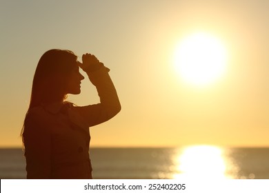 Side view of a silhouette of a woman looking forward at sunset on the beach