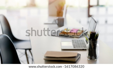 Side view of simple co working space with laptop, office supplies and stationery on desk with chair and blurred background 
