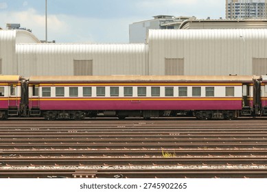 Side view of a single old second class non air conditioned red and white passenger carriage in warm day light 