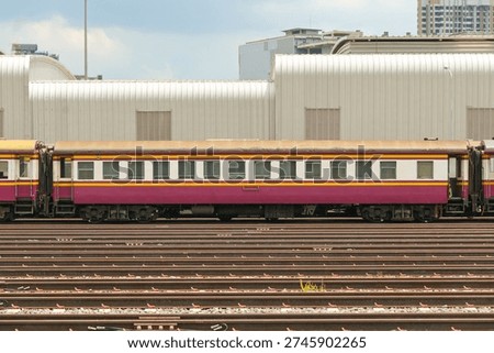 Side view of a single old second class non air conditioned red and white passenger carriage in warm day light 