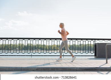 Side View Of Slender Senior Woman Jogging On Bridge