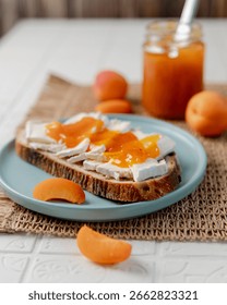 Side view of a slice of fresh bread topped with homemade apricot jam and creamy Brie cheese. Bright and appetizing food photography, ideal for breakfast recipes, brunch, homemade spreads, or culinary content.