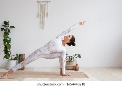 Side view of slim pretty positive young brunette woman doing Utthita parsvakonasana exercise, Extended Side Angle pose, on mat on floor surrounded by houseplants on white wall. Yoga and pilates - Powered by Shutterstock