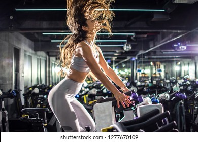 Side view of slim sporty young woman riding exercise bike on cycling training at gym