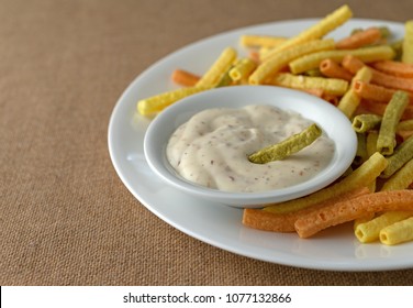 Side view of a small bowl filled with bacon ranch dressing and a green veggie straw atop a plate filled with more food.