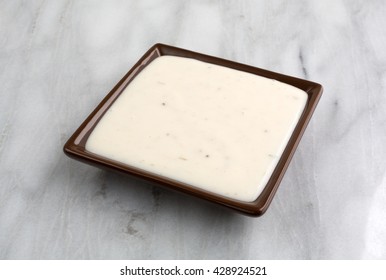 Side View Of A Small Dish Of Creamy Italian Salad Dressing On A Marble Table Top.