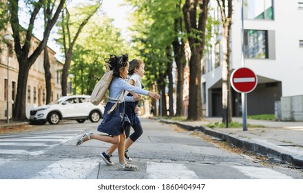 Side view of small school girls crossing street outdoors in town, running. - Powered by Shutterstock