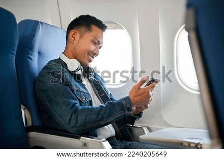 side view, Smart and handsome adult Asian male passenger using his smartphone during the flight.