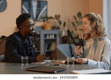 Side view of smiling African American male host discussing politics with young Caucasian female guest during online podcast in studio - Powered by Shutterstock