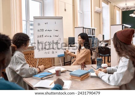 Side view of smiling Asian woman as female teacher teaching Chinese language class to students by whiteboard in library
