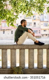 Side view of smiling bearded man sitting on fence under trees.Summer time